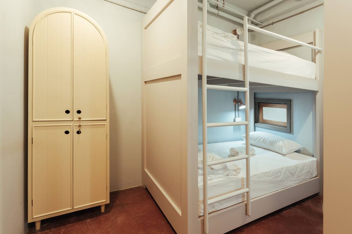 A bunk bed with a ladder, a wardrobe, and a window.