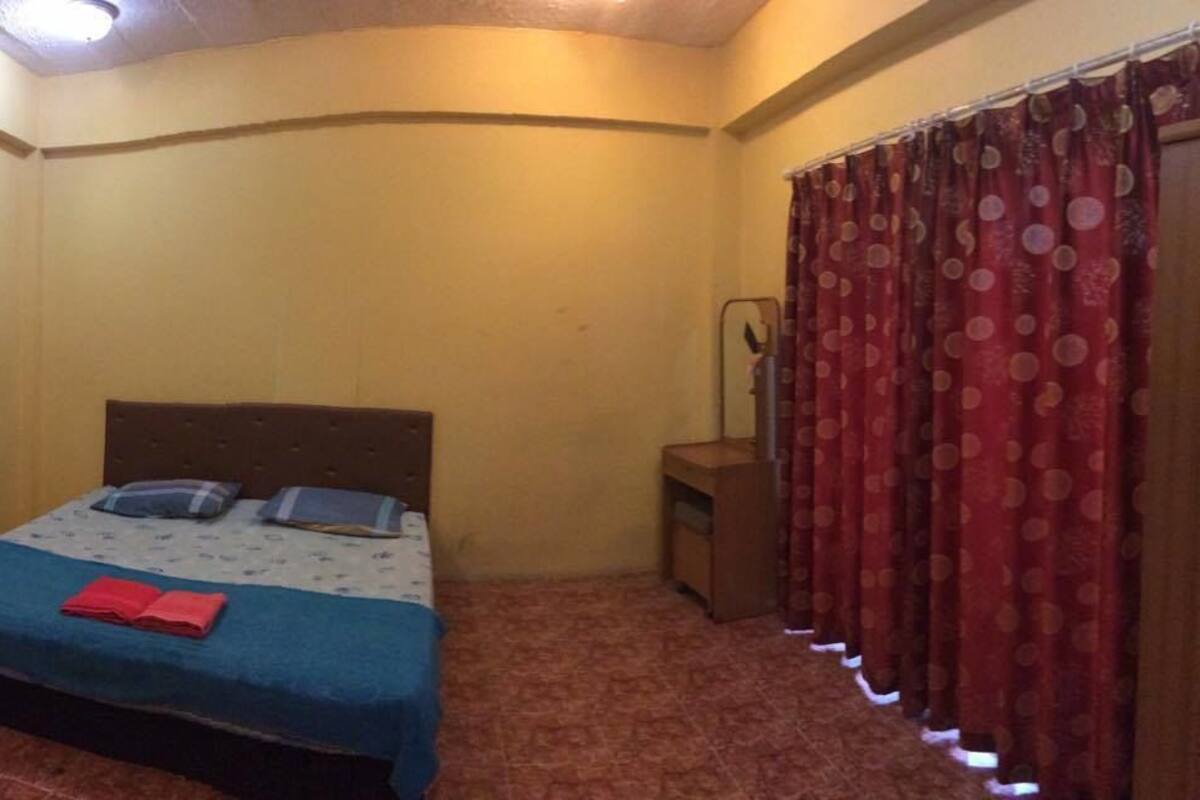 A small, single-bed room with a wooden headboard, a bedside table, and a red curtain.
