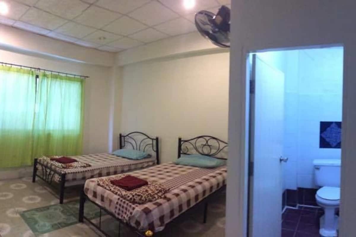 A room with two beds, a toilet, and a window with curtains.