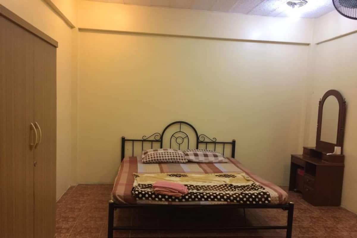 A bedroom with a bed, a wooden wardrobe, a mirror, and a small table.