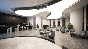Un vestíbulo moderno con un mostrador de recepción curvo, zona de estar con sofás y sillones, y un bar.
