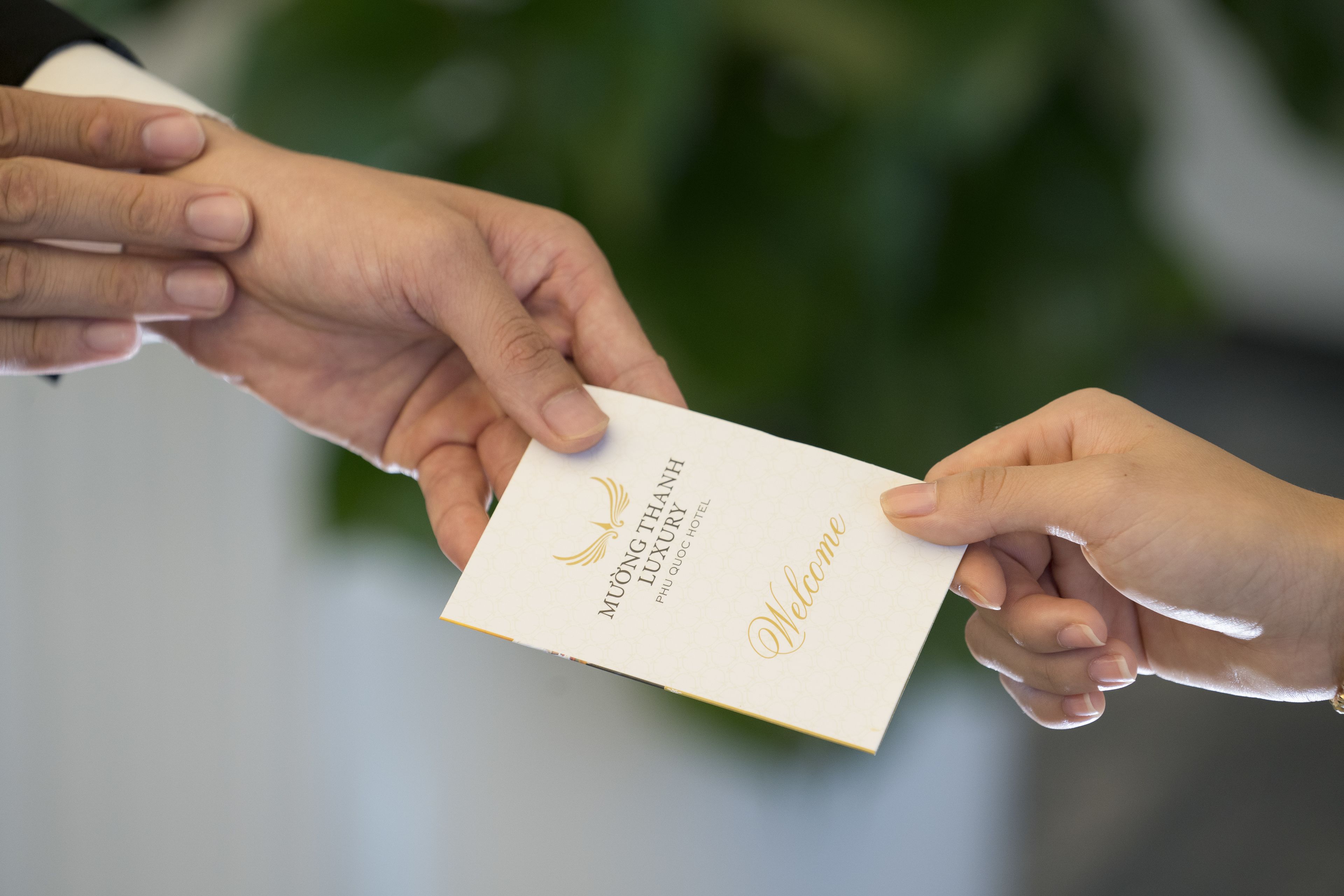 Une main tenant une carte blanche sur laquelle sont écrits les mots « MUONG THANH LUXURY PHU QUOC HOTEL » et « Bienvenue ».