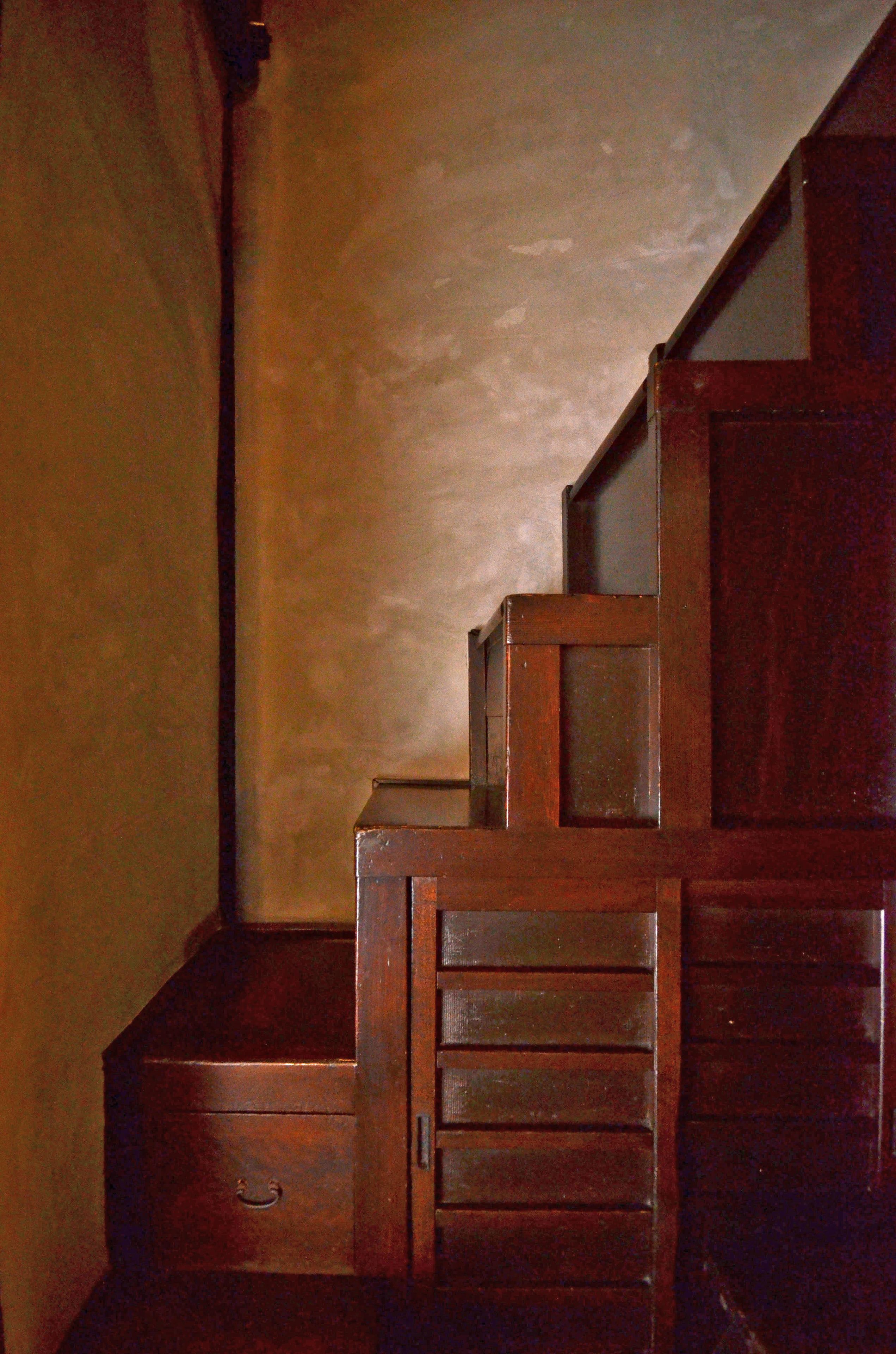 Eine Holztreppe mit Handlauf und einer kleinen Holzbank am Fuß.