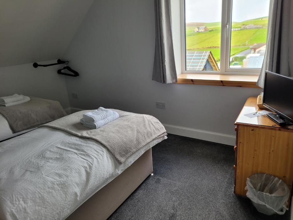 A bedroom with a bed, a desk with a computer, a window with a view of the countryside, and a hanging coat rack.