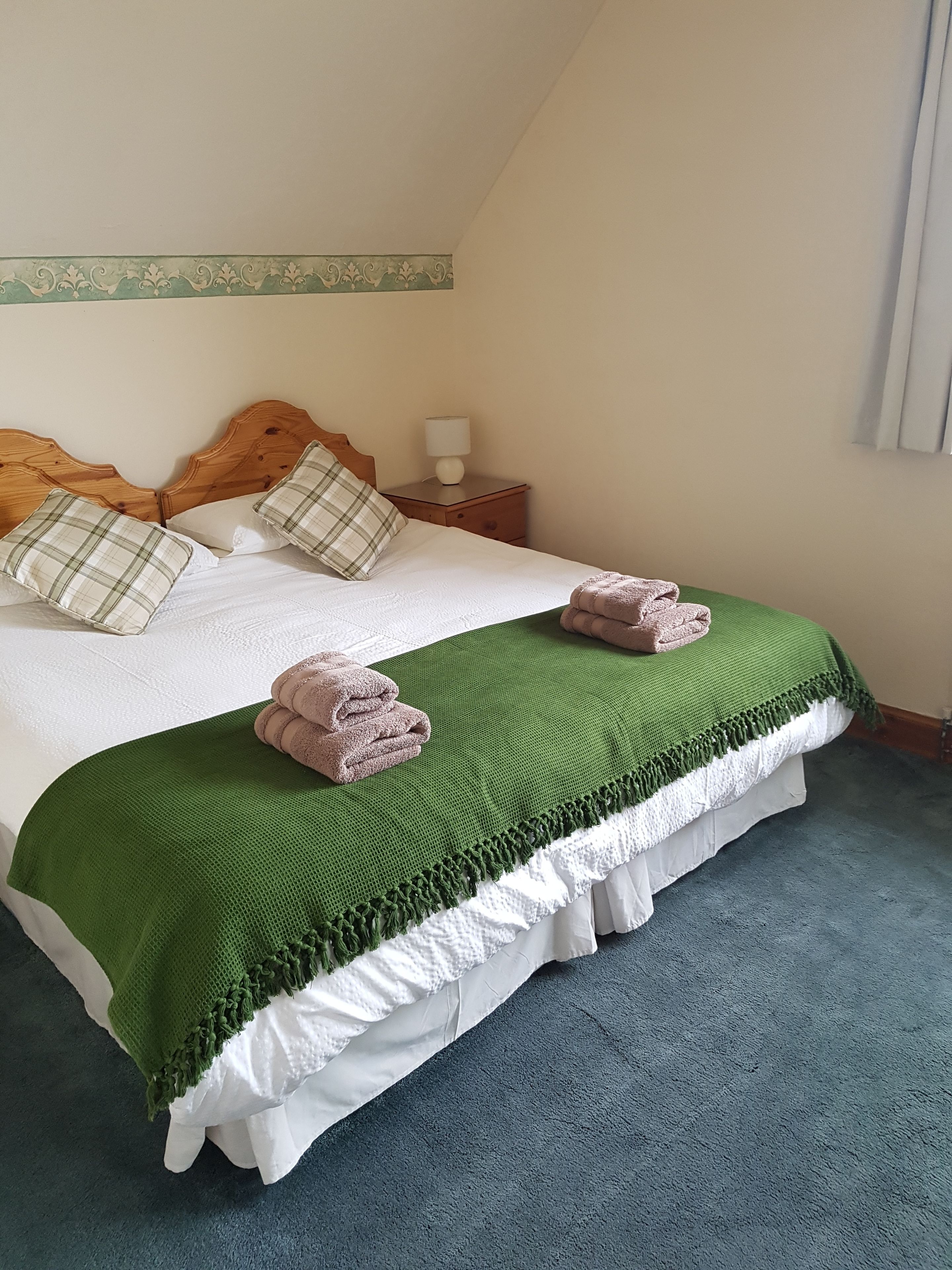 A neatly made bed with a green blanket, two pillows, and folded towels.