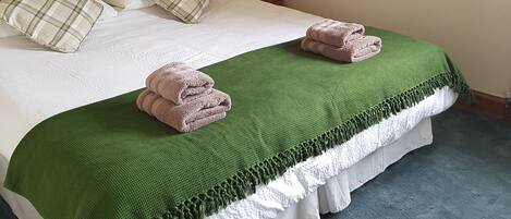 A neatly made bed with a green blanket, two pillows, and folded towels.