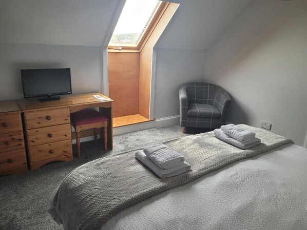 A bedroom with a bed, a desk with a computer, a chair, and a window.