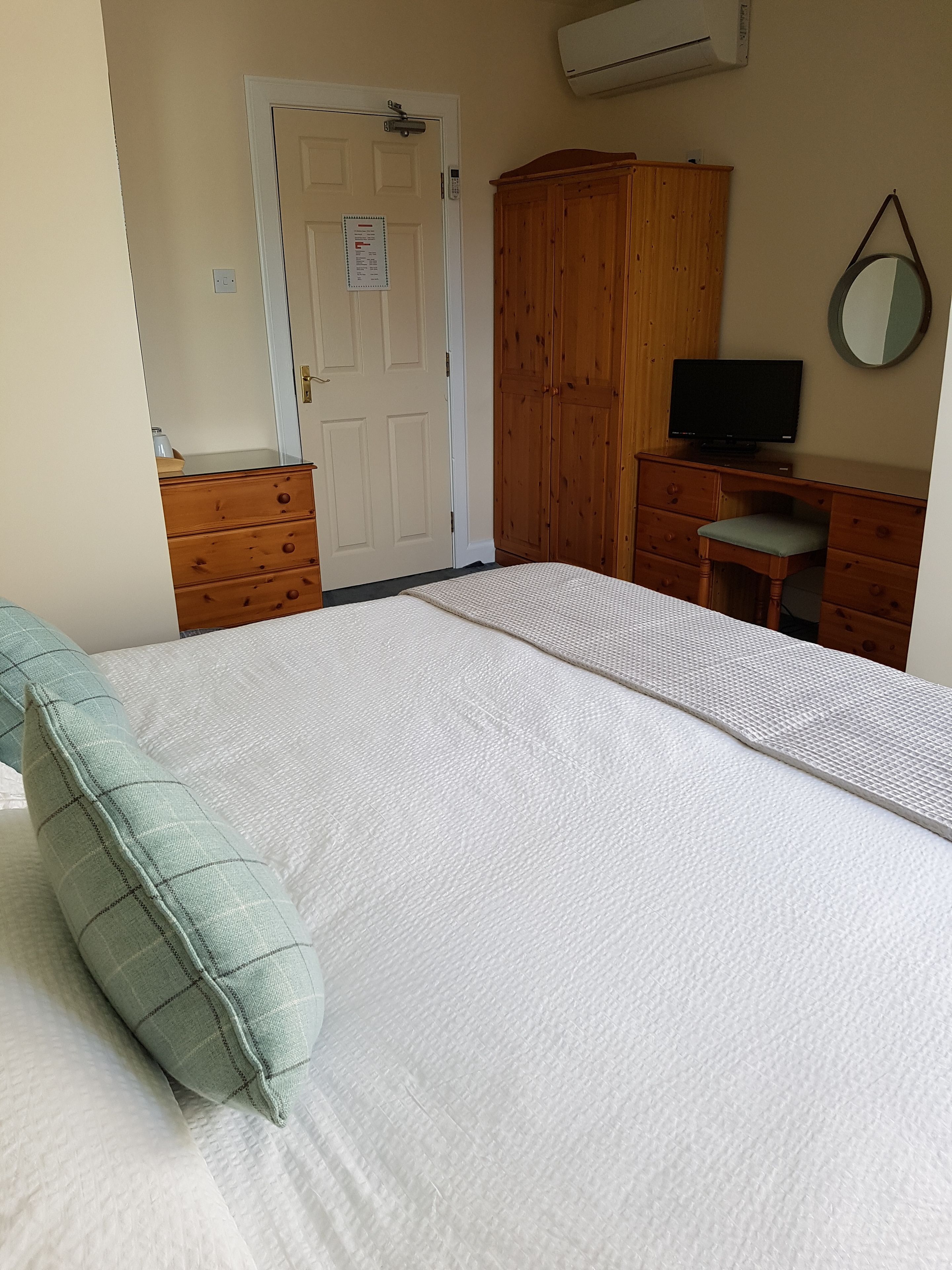 Ein Schlafzimmer mit einem Bett, einem Holzschrank, einem Schreibtisch mit Stuhl, einem Fernseher und einem Spiegel an der Wand.
