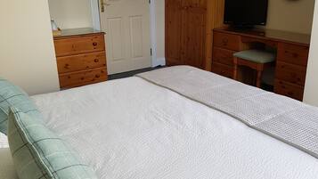 Ein Schlafzimmer mit einem Bett, einem Holzschrank, einem Schreibtisch mit Stuhl, einem Fernseher und einem Spiegel an der Wand.