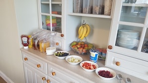 Una encimera de cocina con diversos alimentos y utensilios, incluyendo un frutero, un recipiente con jugo y un bote de yogur griego.