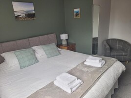 Una cama bien hecha con almohadas y toallas dobladas, una lámpara de noche y una silla.