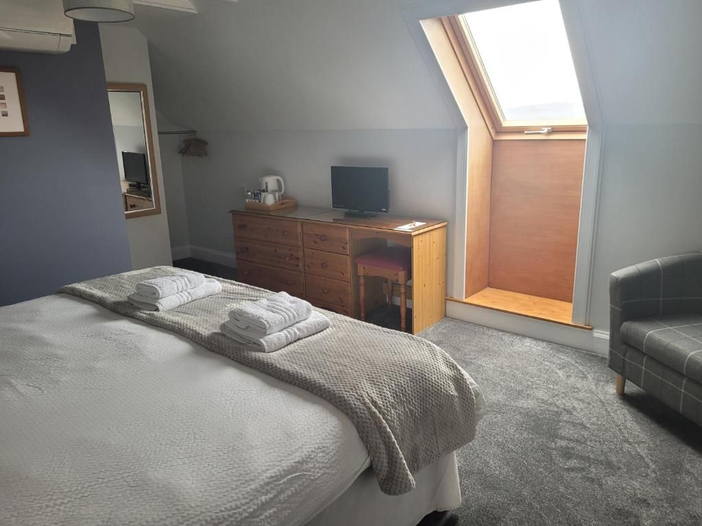 A bedroom with a bed, a desk with a television, a chair, and a window.