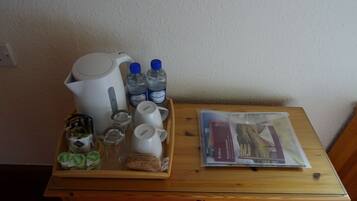 Une table en bois sur laquelle se trouve un plateau contenant une bouilloire, deux bouteilles d’eau, une tasse, un verre, un pot de yaourt et un paquet de biscuits.