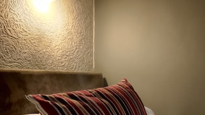 Un lit bien fait, avec du linge de lit blanc et un coussin à rayures, un mur à texture et un luminaire fixé au mur.