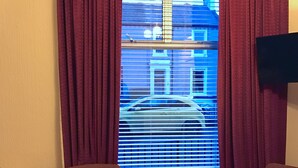 Une chambre d’hôtel dotée d’une grande fenêtre, de deux fauteuils, d’une commode et d’un téléviseur fixé au mur.