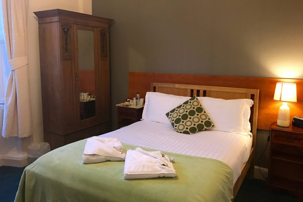 Ein Hotelzimmer mit einem Bett, einem Holzschrank, einem Nachttisch mit Lampe und einer grünen Bettdecke.