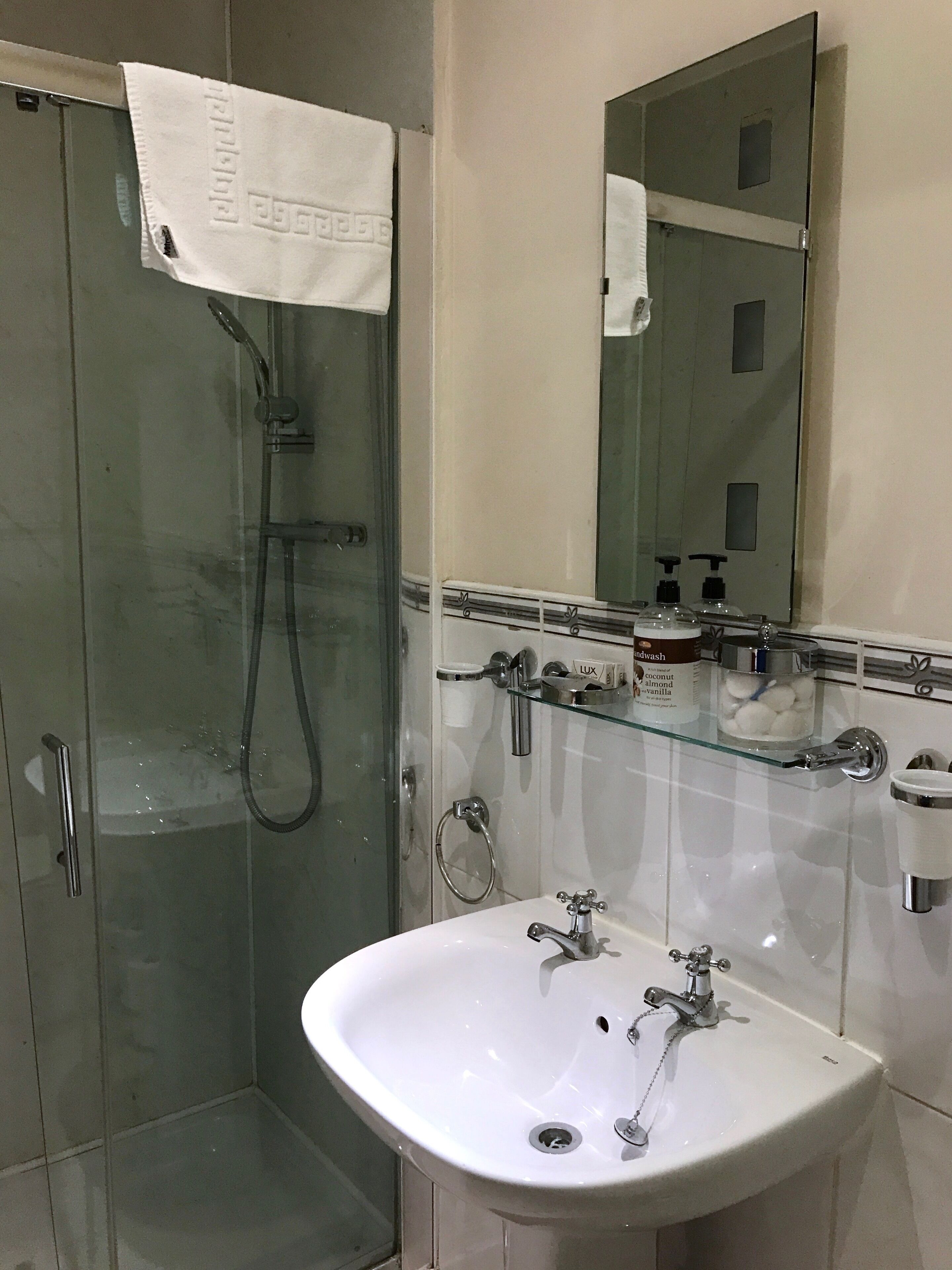 A bathroom with a glass shower enclosure, a white sink with a mirror above it, and toiletries on the countertop.
