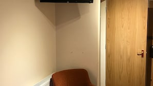 Une pièce avec un téléviseur fixé au mur, un radiateur, une porte en bois et un lit rouge.