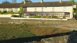 Un bâtiment traditionnel doté d’une grande baie vitrée, de murs en pierre et d’un champ verdoyant au premier plan.