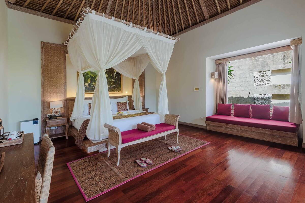 Un dormitorio con cama con dosel, un sofá, suelo de madera y vistas al exterior.