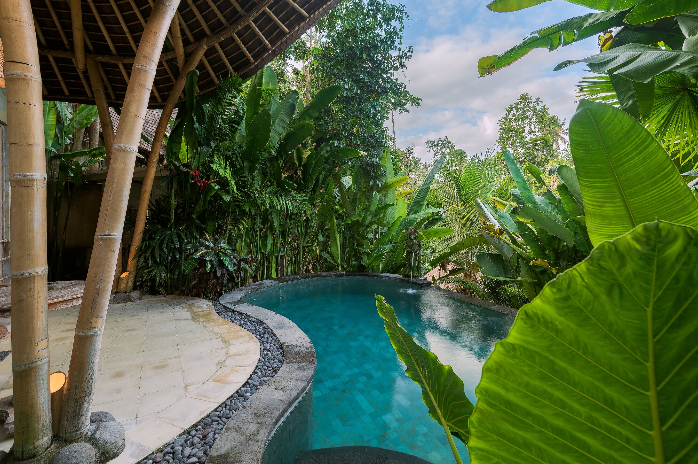 A pool surrounded by lush greenery and bamboo structures.