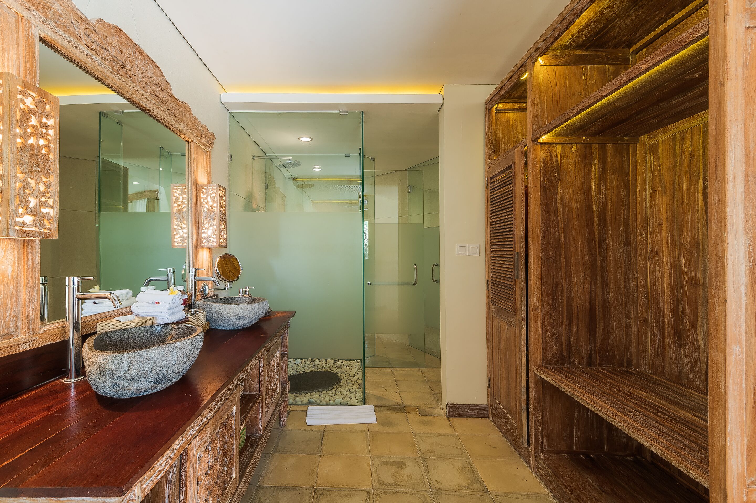 Une salle de bain dotée d’un grand miroir, de deux vasques en pierre, d’une douche à parois de verre et de meubles en bois.