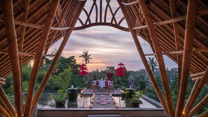 A bamboo-framed outdoor dining area with a sunset view, a table set for two, and decorative lanterns. - The Udaya Resorts and Spa (Ubud)