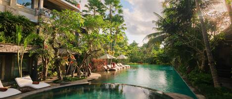 A pool area with lounge chairs and umbrellas, surrounded by lush greenery and palm trees.