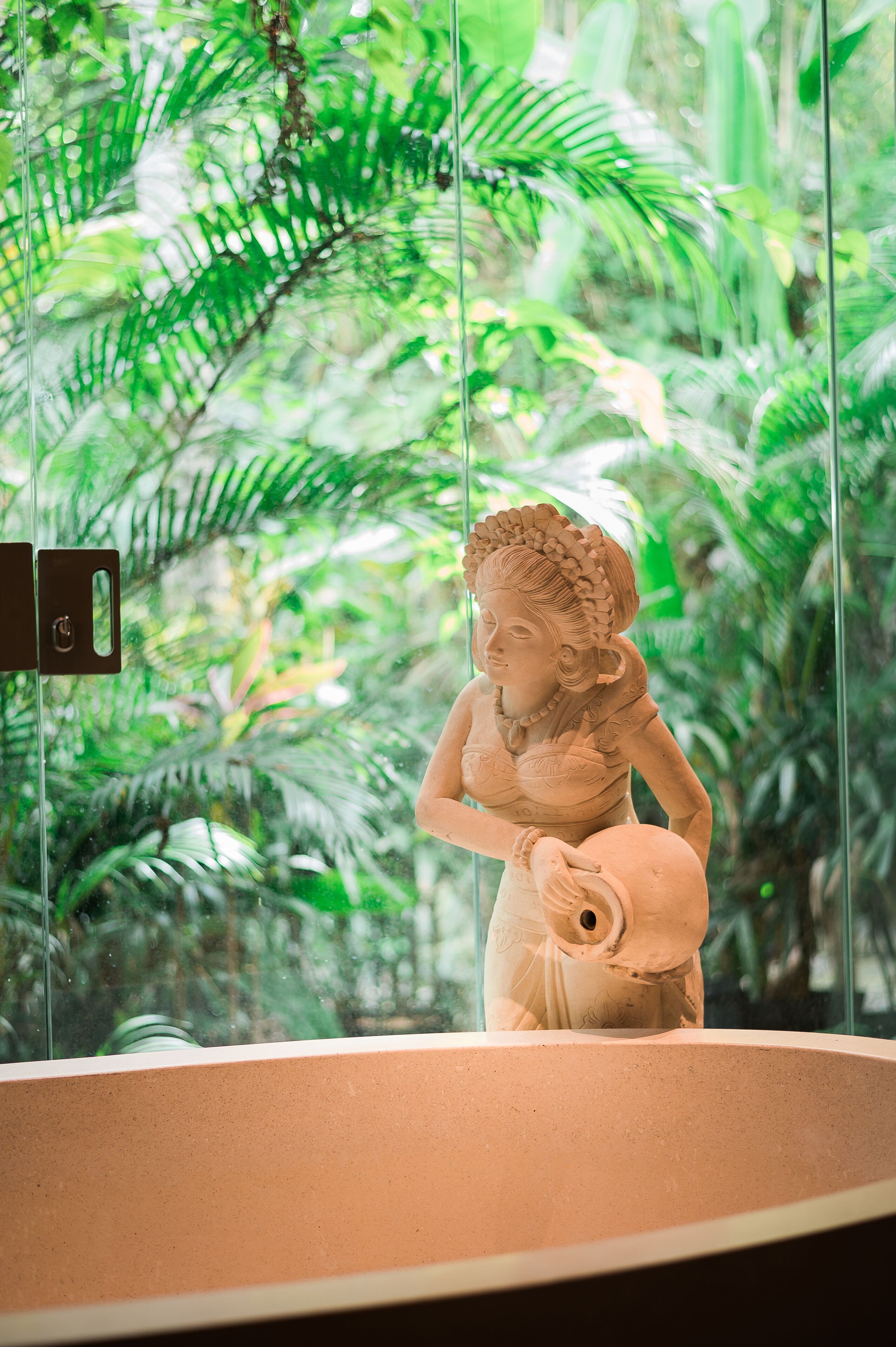 Una estatua de una mujer en un museo, dentro de un recinto de vidrio, rodeada de abundante follaje verde.