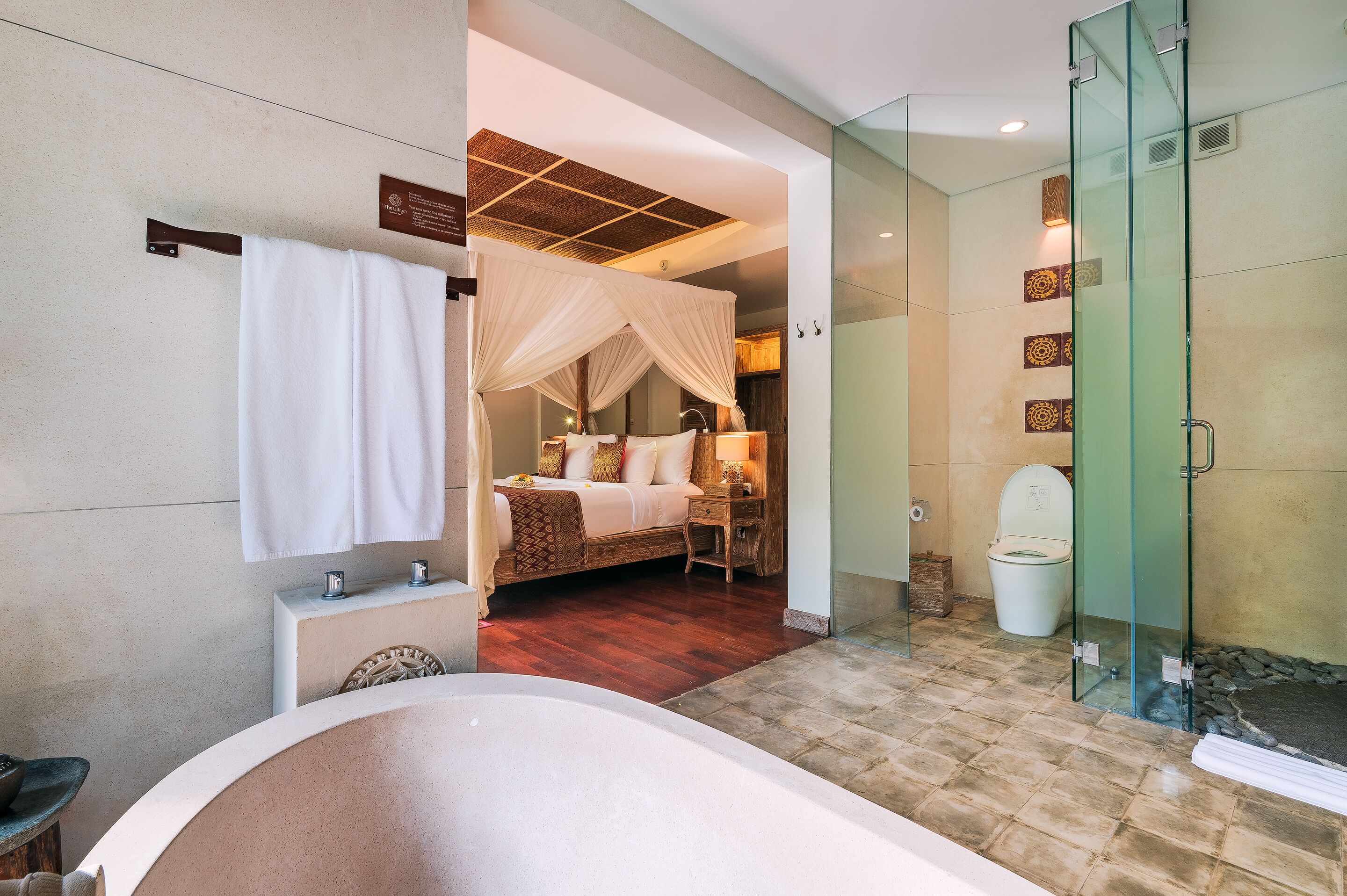 Un baño moderno con una bañera grande, ducha con mampara de vidrio y un dormitorio separado con cama a dosel.