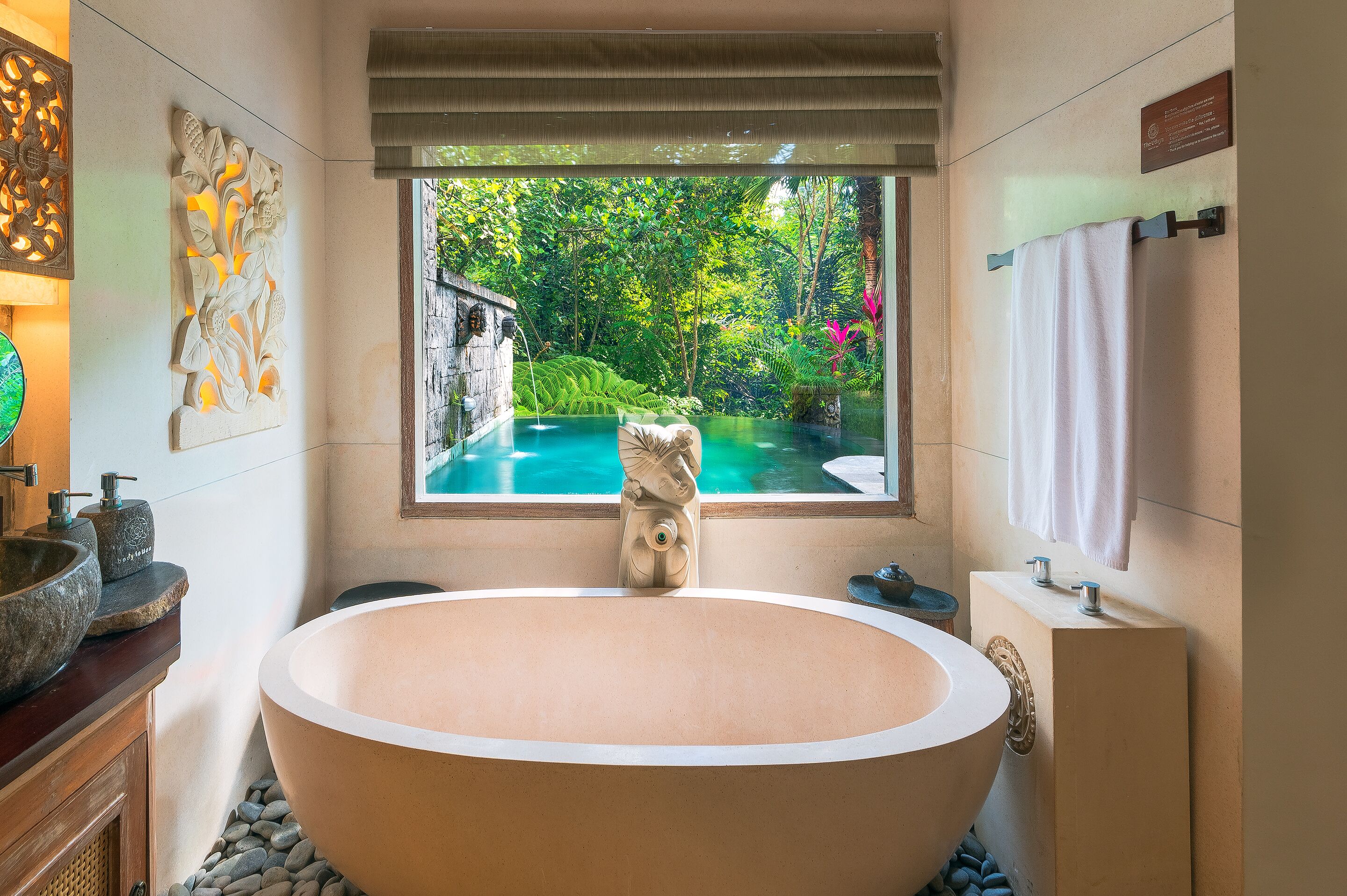 Un baño con una bañera grande independiente, una ventana con vista a un jardín exuberante y un lavabo de piedra.