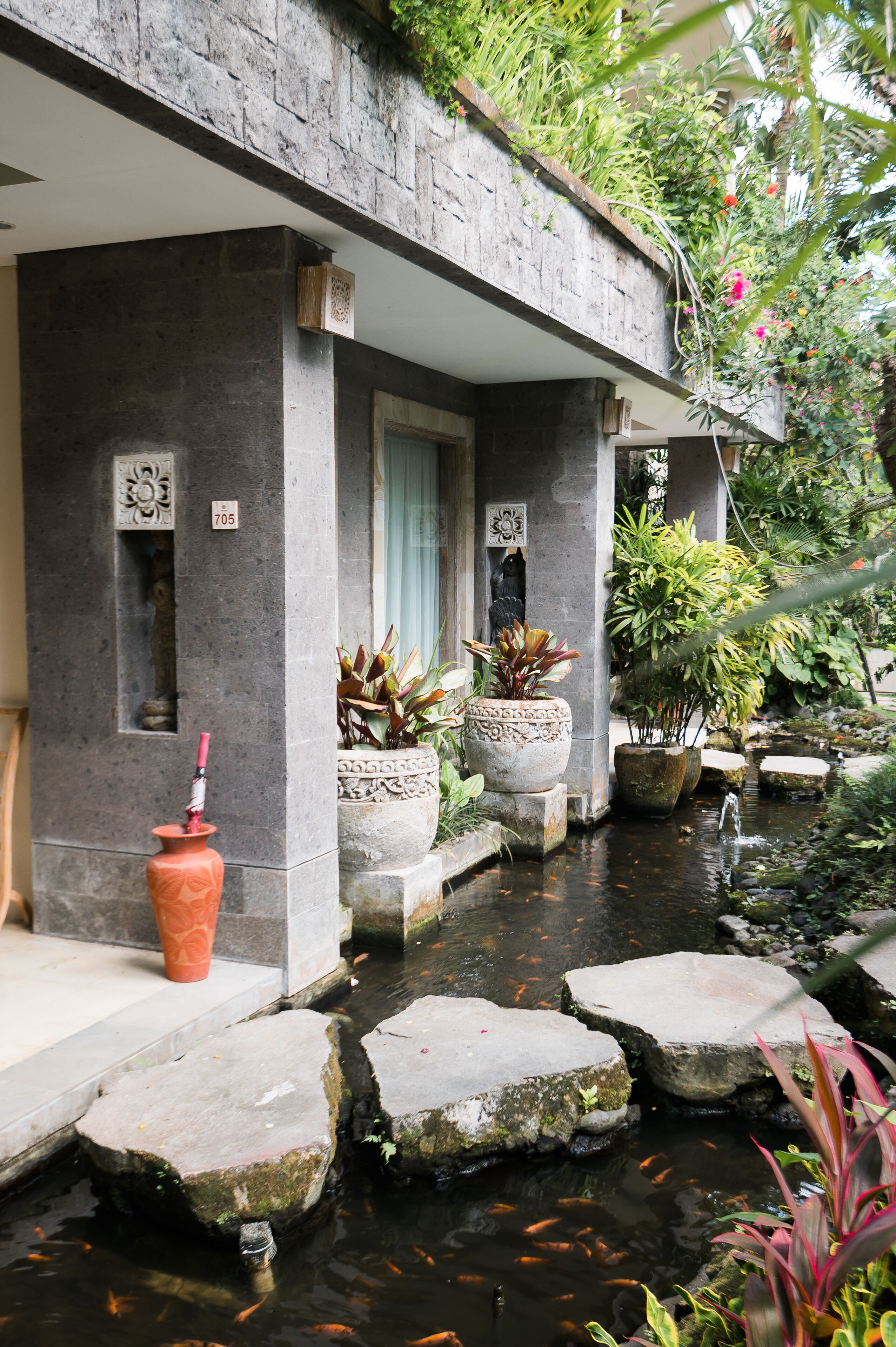 A stone building with a water feature, potted plants, and a koi pond.