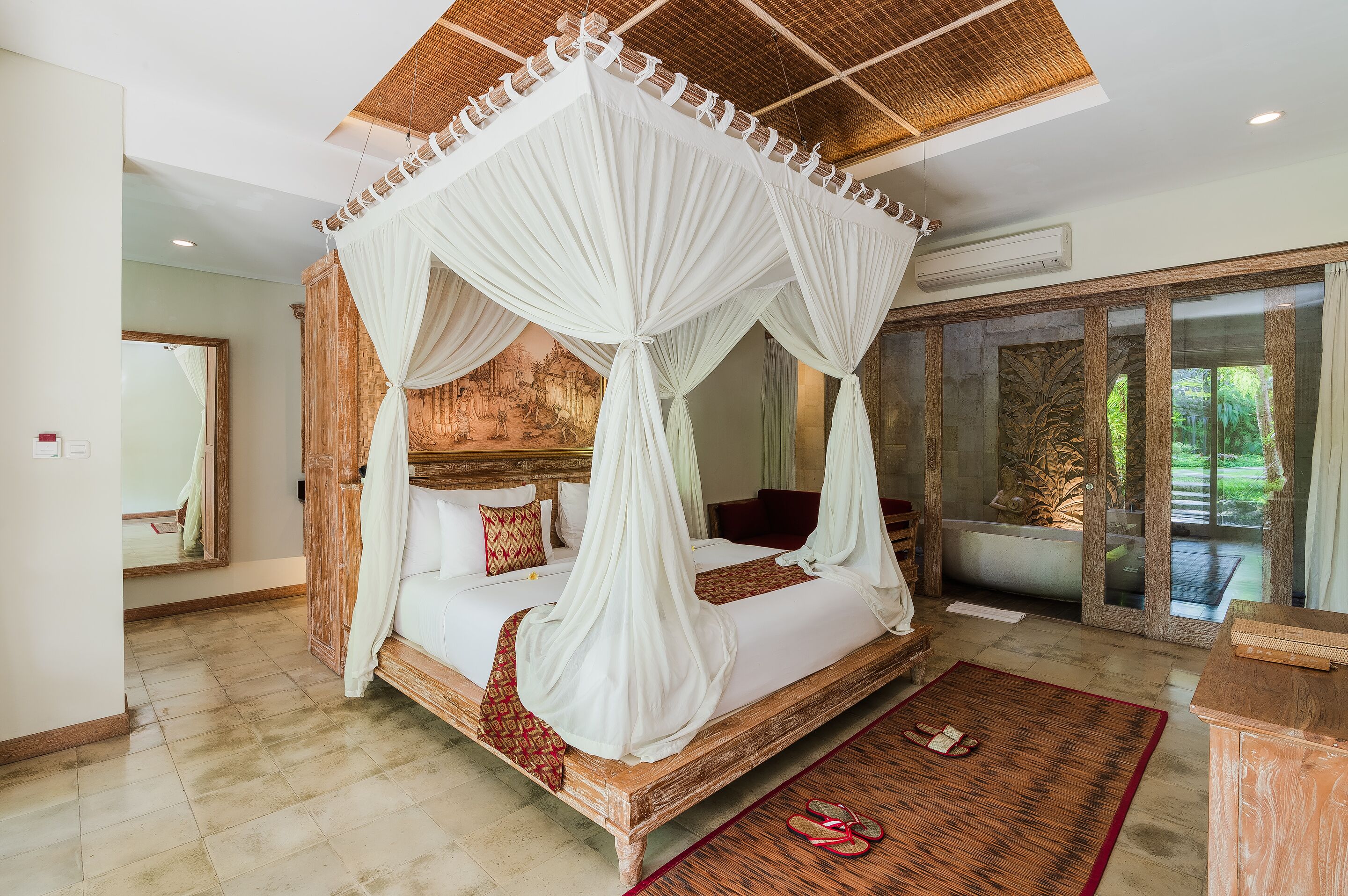 A four-poster bed with a canopy, a large mirror, and a view of a garden through a glass door.