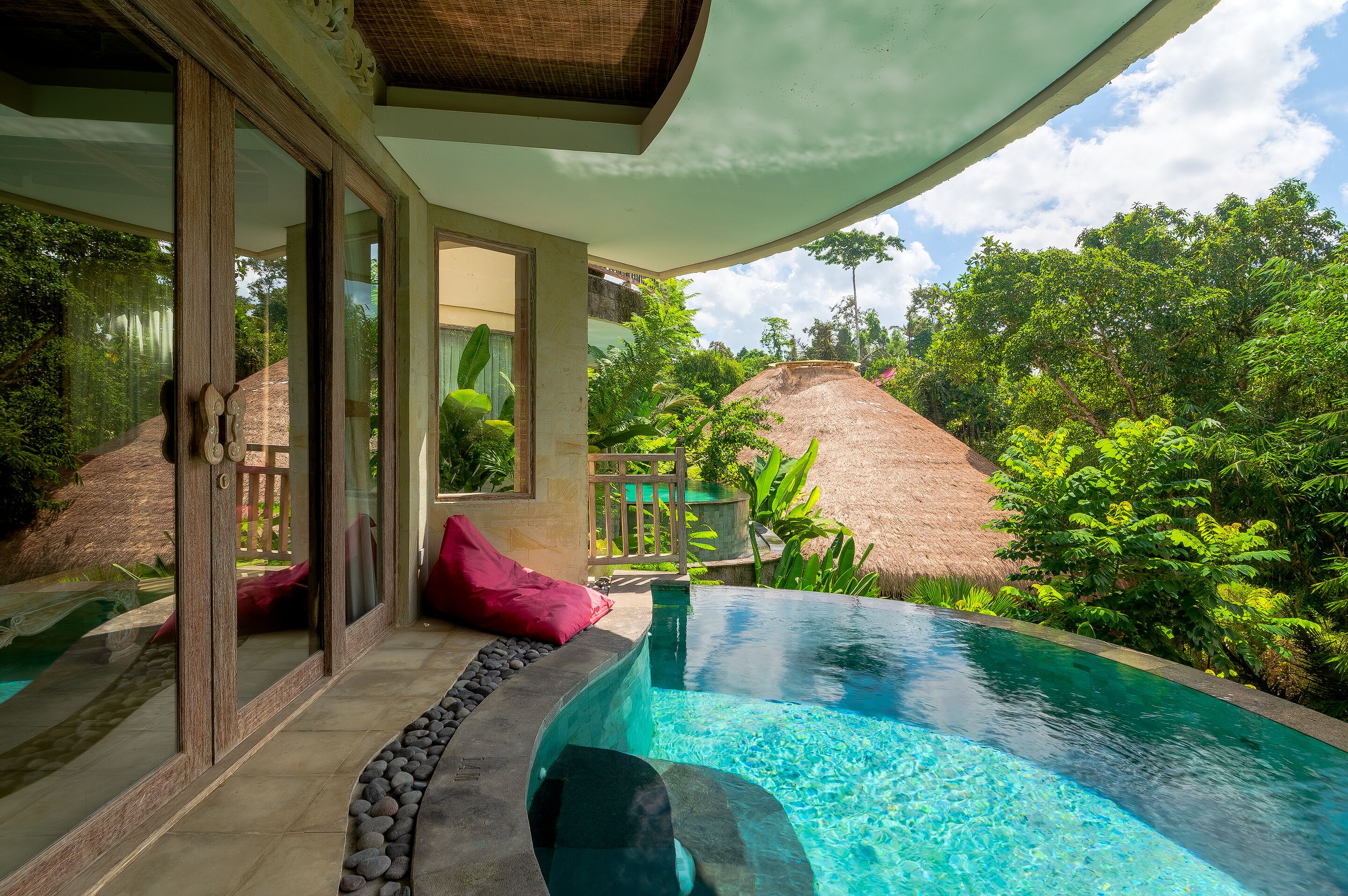 A private pool area with a glass enclosure, a thatched roof structure, and lush greenery surrounding the property.