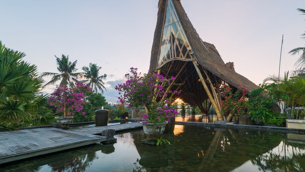 A resort with a unique thatched-roof structure, a calm pool, and lush tropical vegetation. - The Udaya Resorts and Spa (Ubud)