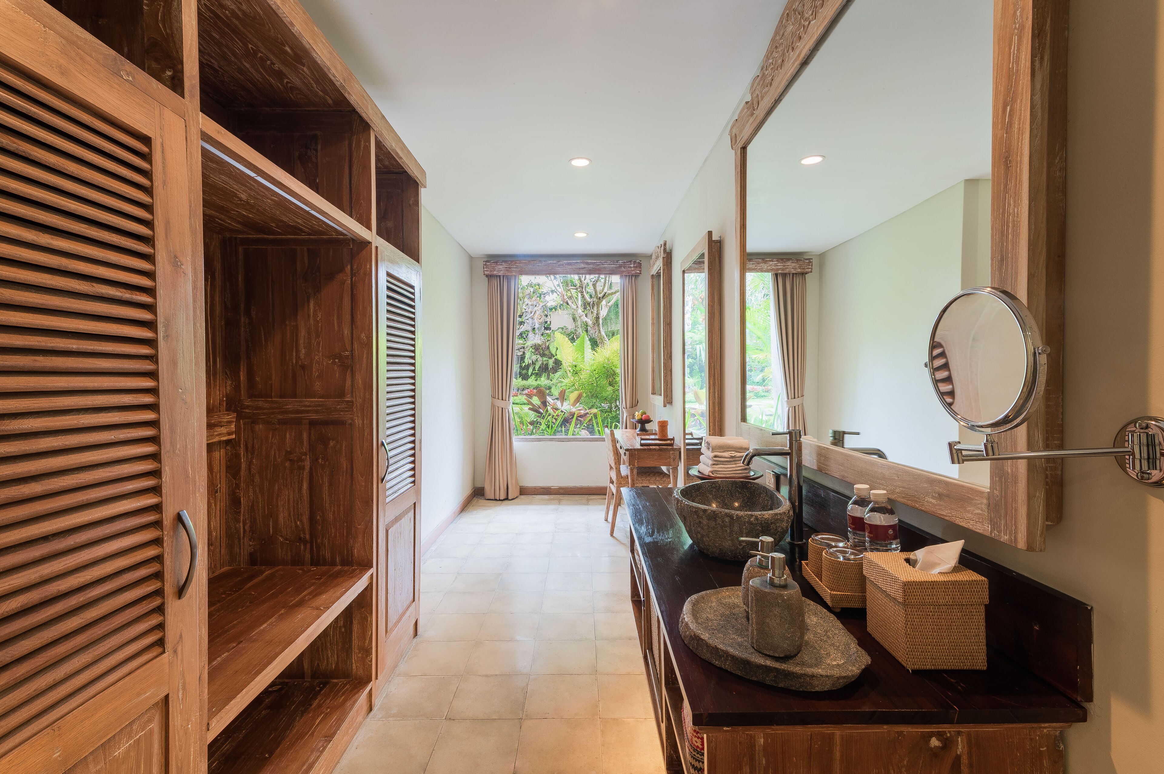 A bathroom with wooden shelves, a large mirror, a stone sink, and a view of greenery outside.