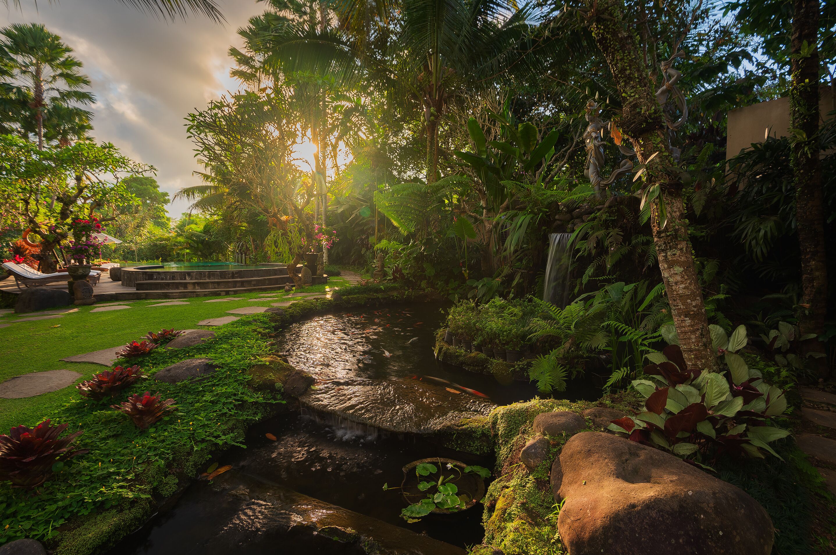 A serene garden with a small stream, lush greenery, and a stone pathway.