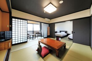Une pièce de style japonais traditionnel, avec un sol recouvert de tatamis, une table basse, un téléviseur et une porte coulissante donnant sur une chambre à coucher.