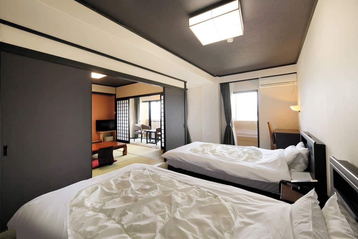 A hotel room with two beds, a desk, a chair, and a television.