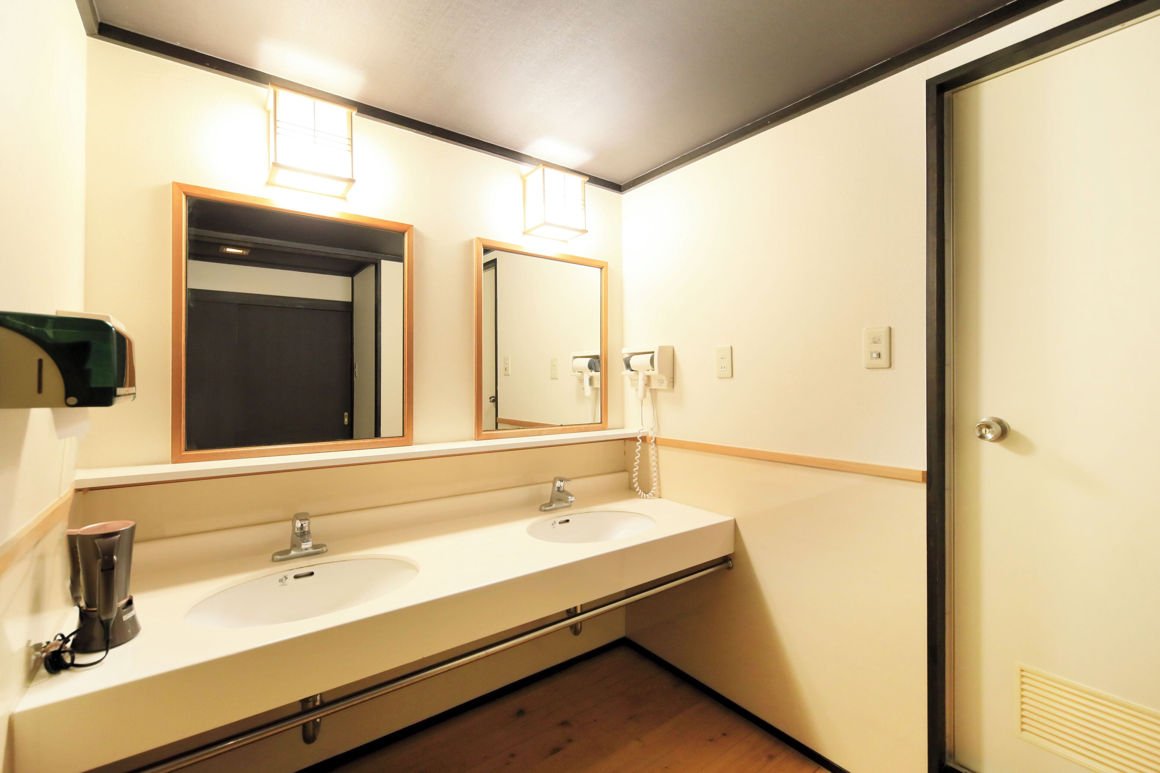 A bathroom with two sinks, a mirror, a towel dispenser, and a door.