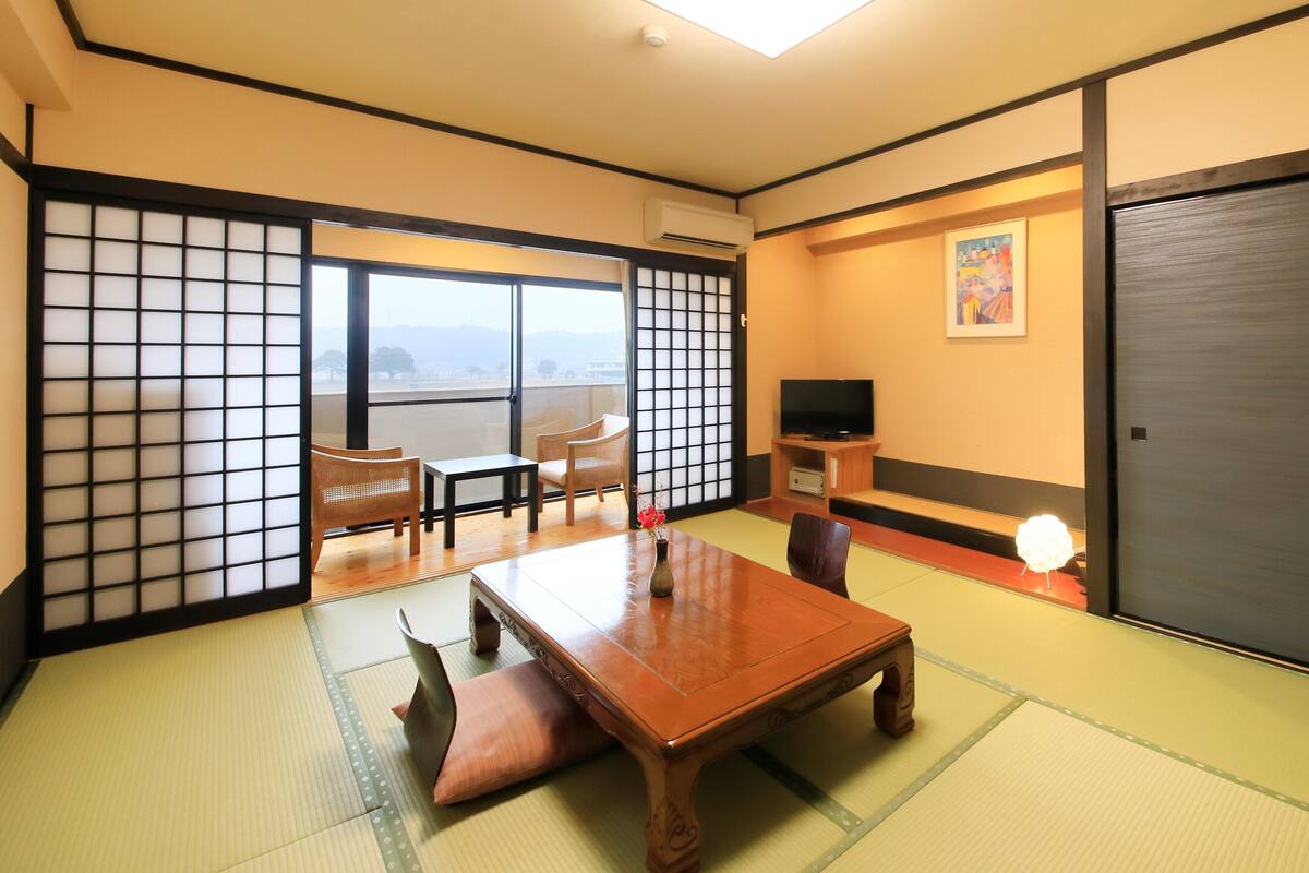 A traditional Japanese room with tatami flooring, a low wooden table, and a television on a shelf.