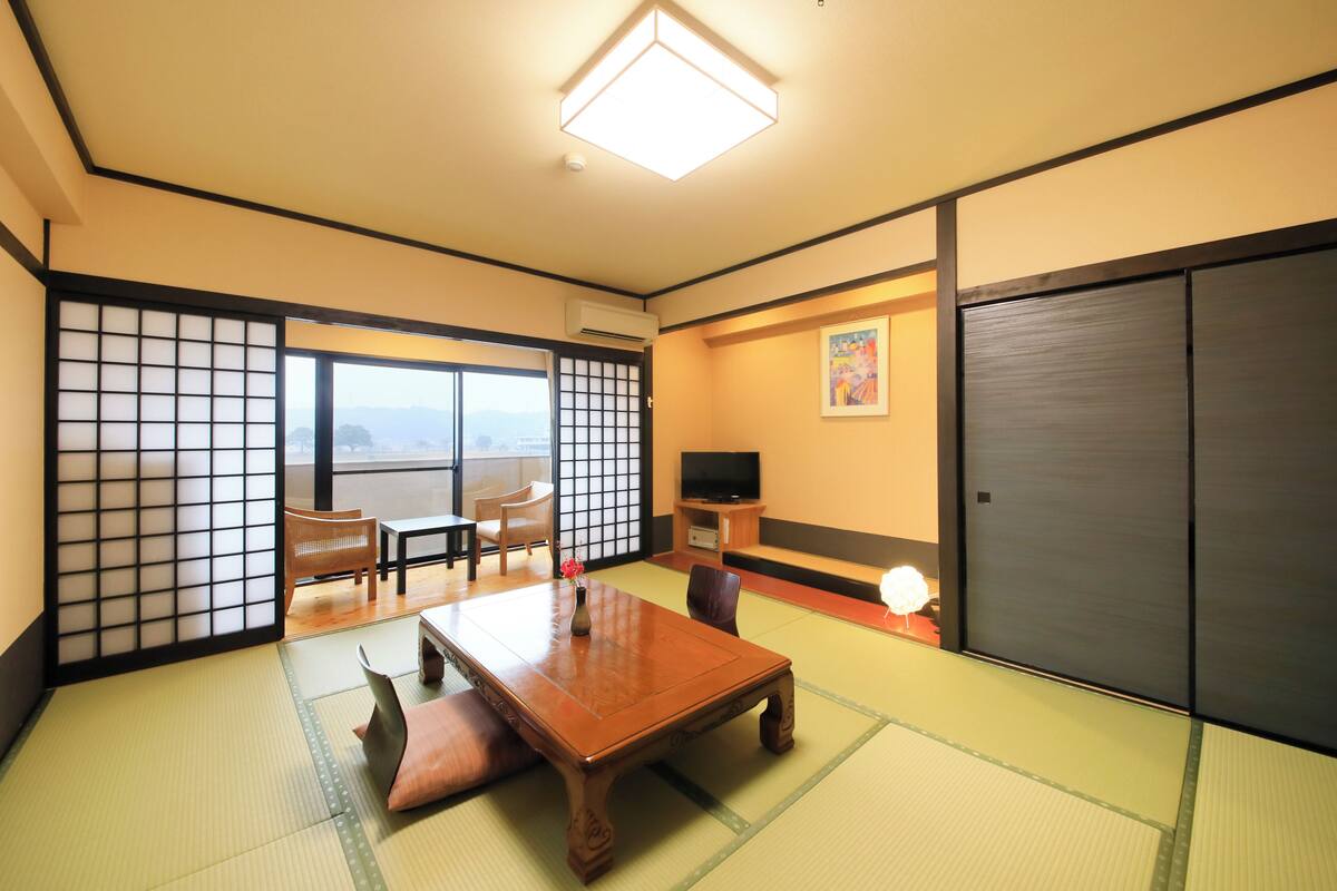 A traditional Japanese room with tatami flooring, a low table, chairs, a TV, and sliding doors.