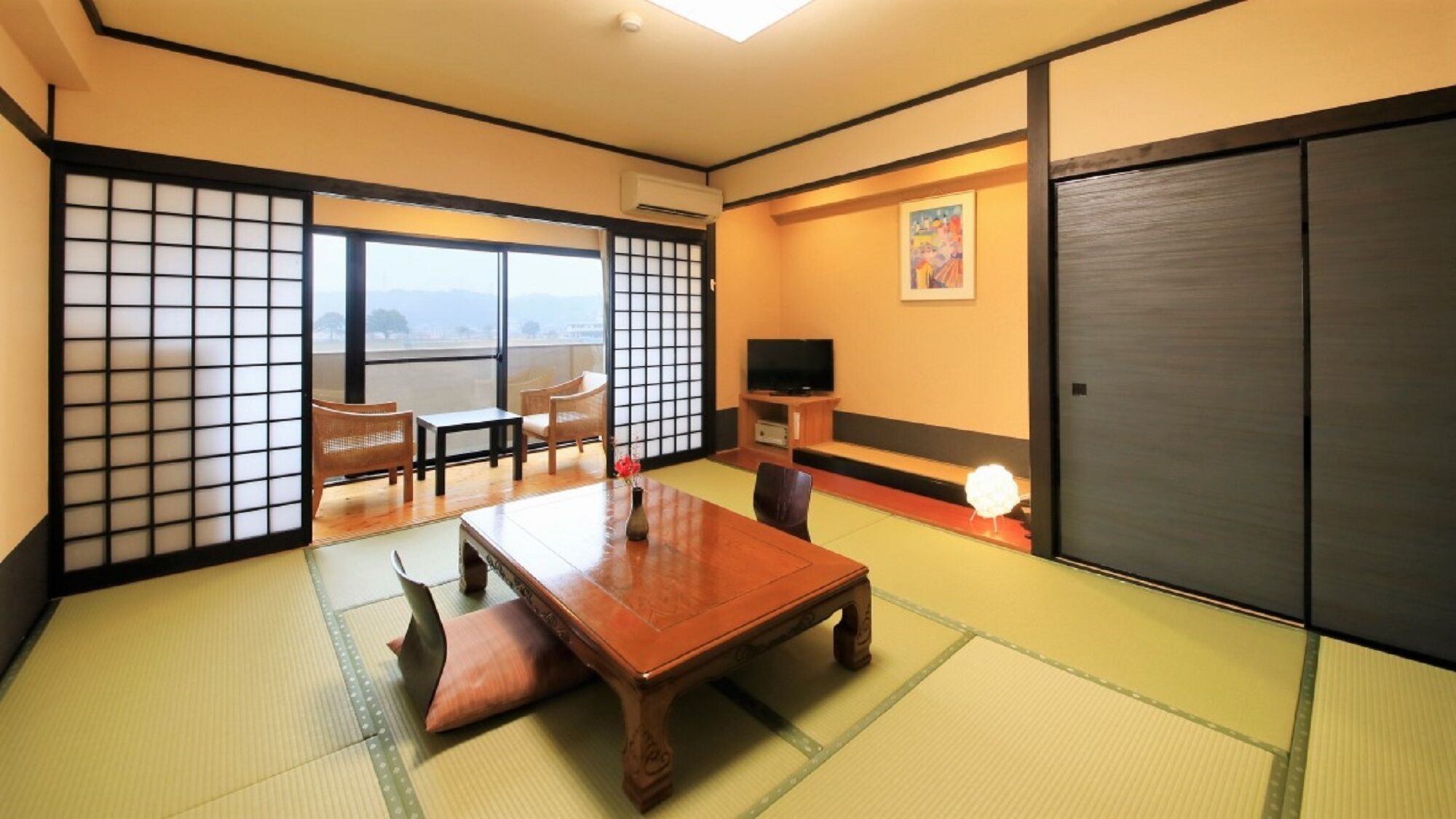 A traditional Japanese room with tatami flooring, a low table, chairs, a TV, and a sliding door.