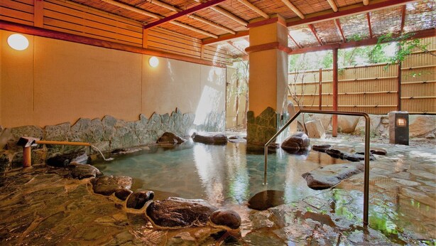 A traditional Japanese onsen with a stone bath surrounded by rocks, wooden beams, and a bamboo roof. - Yutorelo Yamaga (Yamaga)