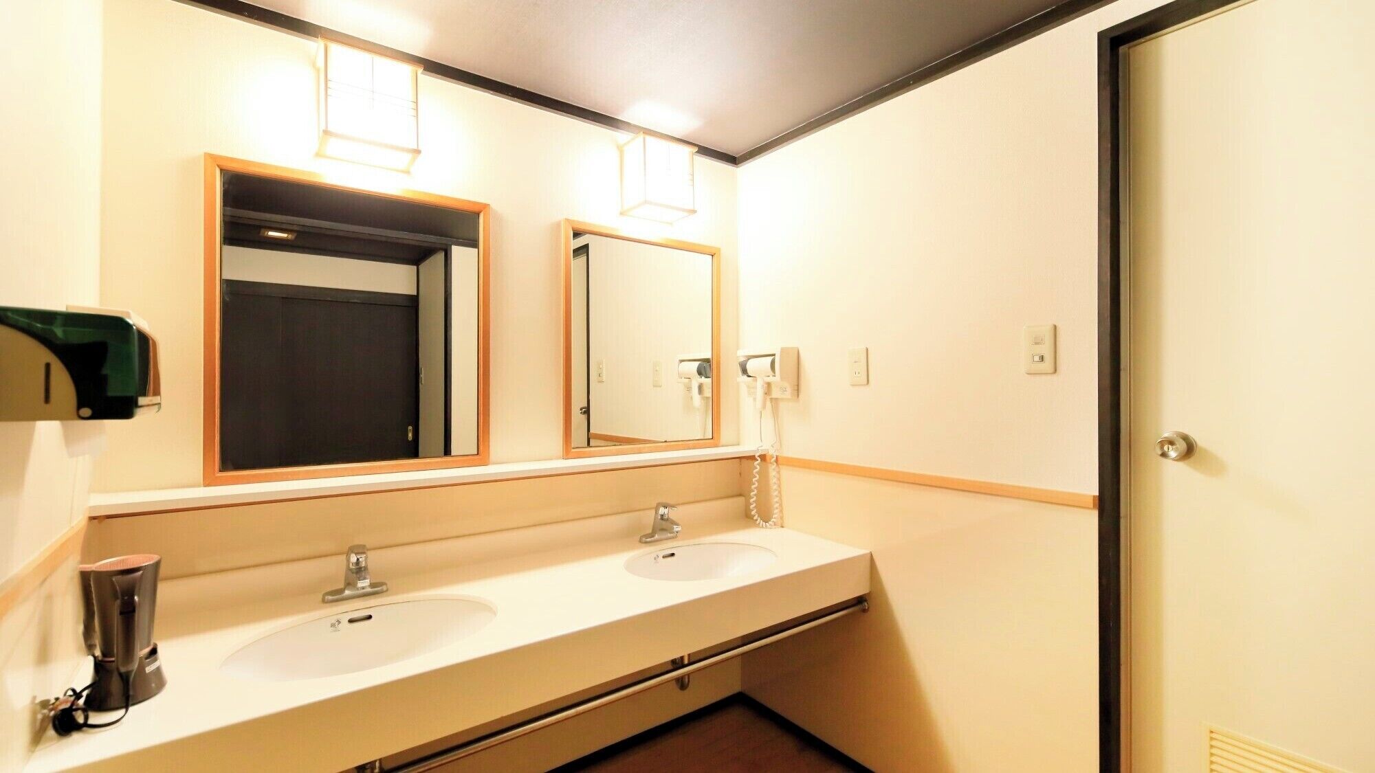 Une salle de bain d’hôtel avec deux lavabos, un miroir, un distributeur de serviettes et une porte.