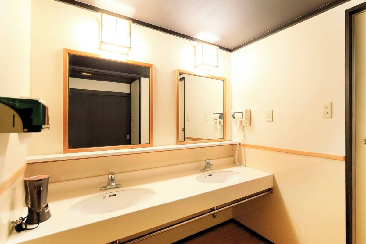 A hotel bathroom with two sinks, a mirror, a towel dispenser, and a door.
