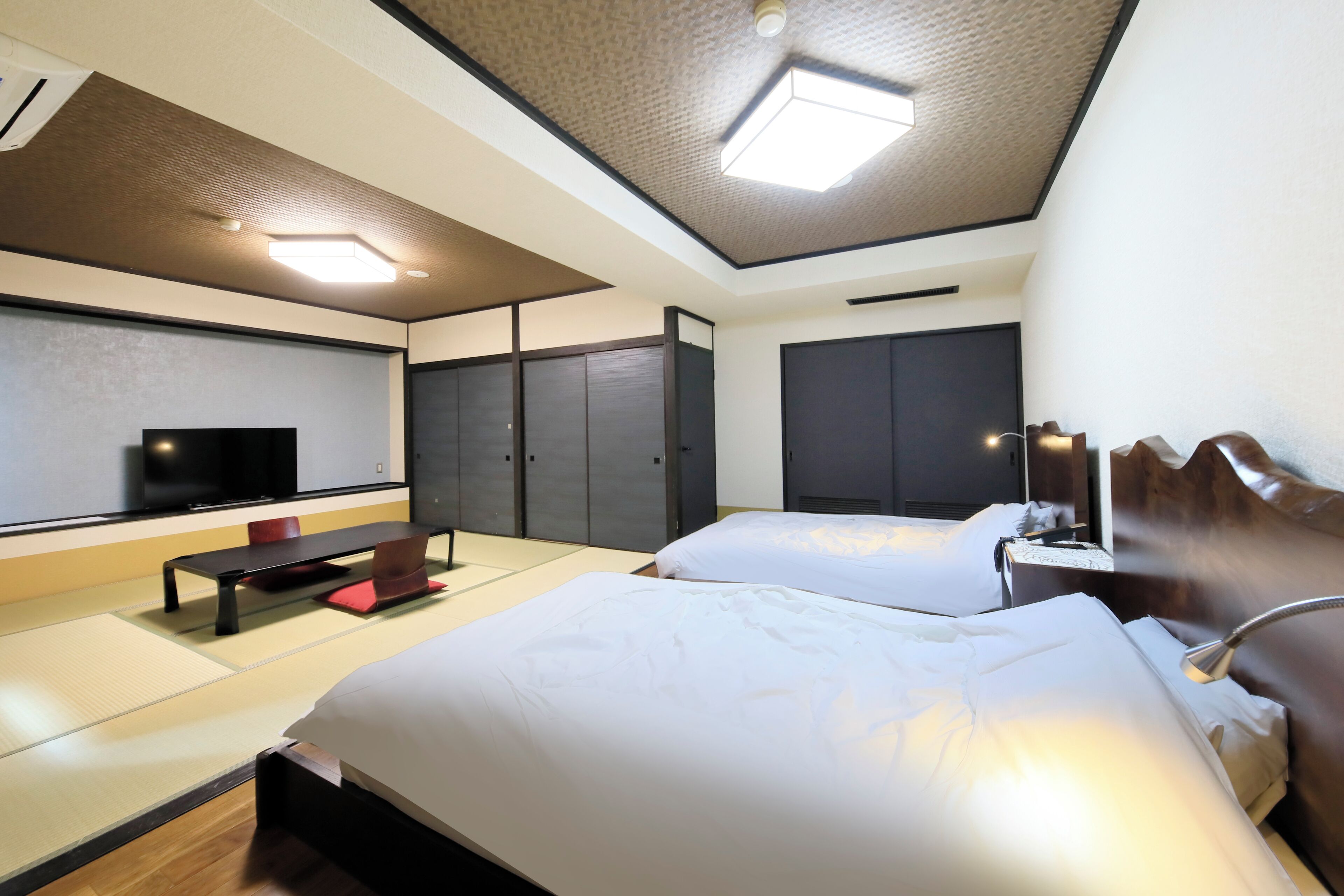 A hotel room with two beds, a TV, a desk with a lamp, and a ceiling light.
