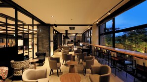 A modern lounge area with multiple seating options, including sofas and chairs, arranged around a central coffee table. Large windows provide a view of the outdoors. - Yutorelo Yamaga (Yamaga)