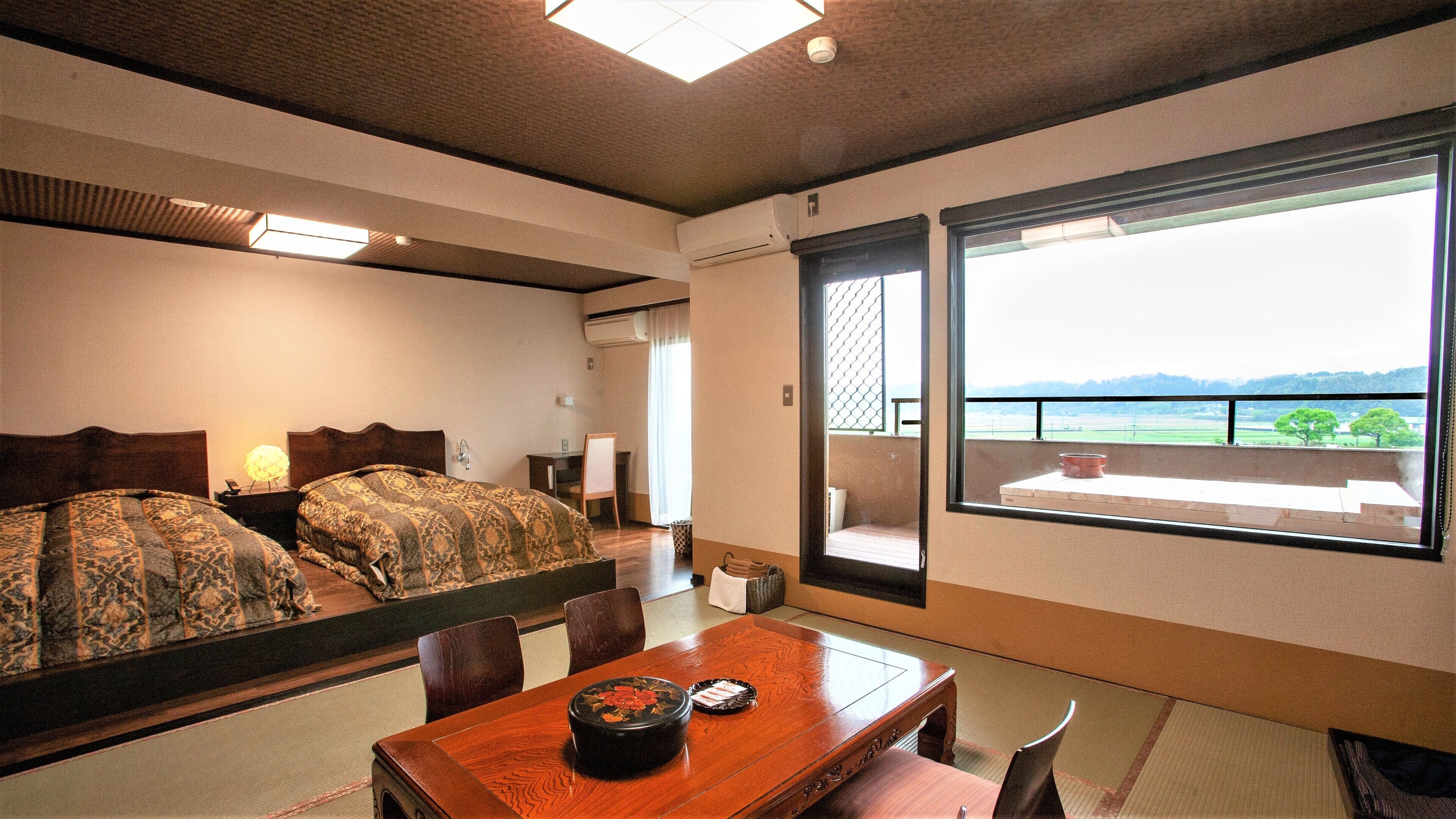 Une chambre d’hôtel avec un lit, une table à manger agrémentée d’un service à thé japonais traditionnel, une vue sur un balcon doté d’une balustrade et un climatiseur fixé au mur.