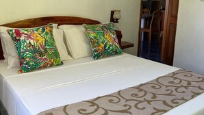 Una cama bien hecha con una colcha estampada y dos almohadas, una con diseño tropical y otra de color liso.